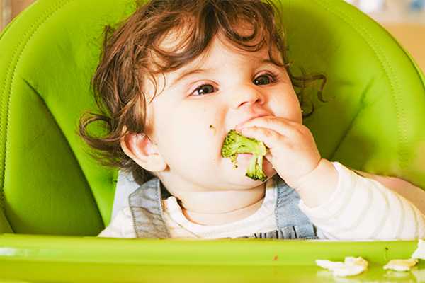 Toddler feeding himself broccoli, demonstrating baby led weaning.